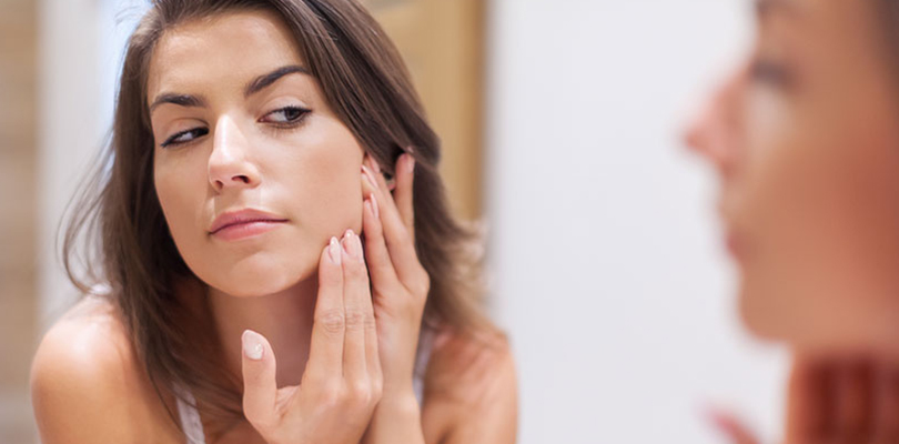 Woman is observing her skin in the mirror